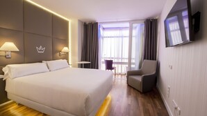 A hotel room with a large bed, a TV mounted on the wall, a chair, and a small table. - Erase un Hotel (Madrid)