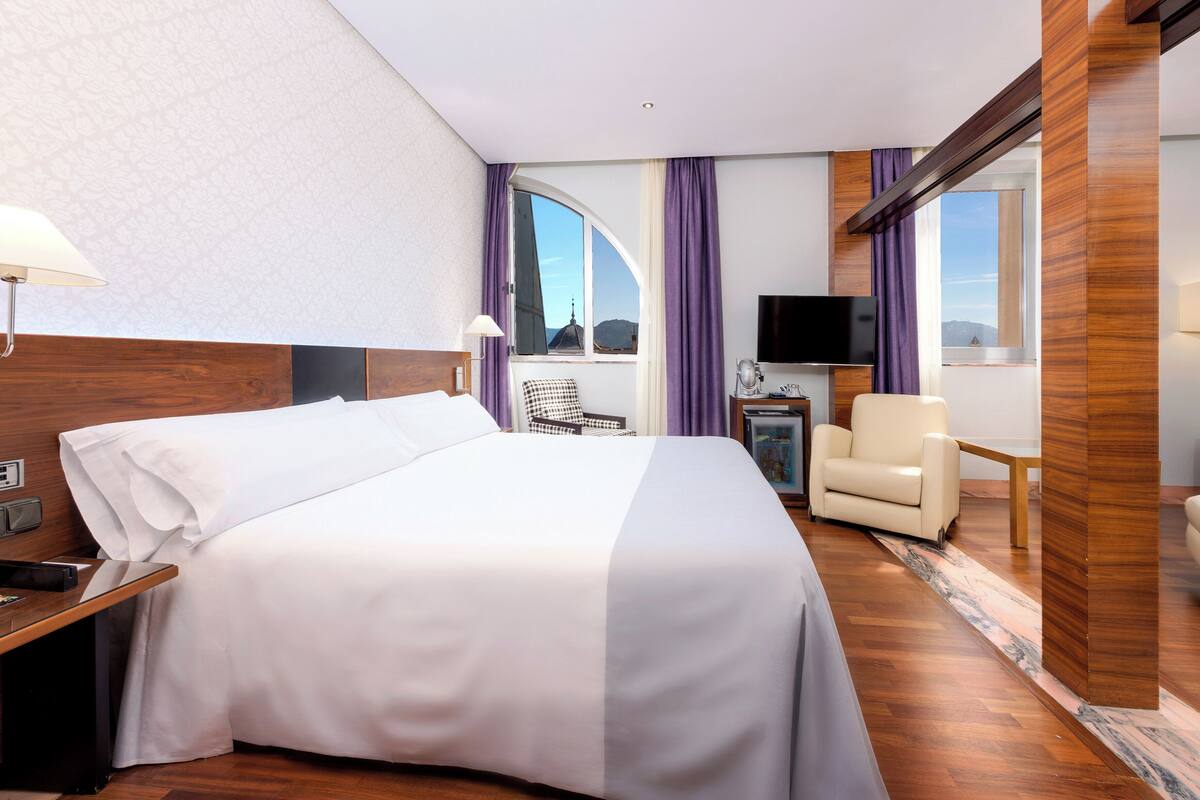Une chambre d’hôtel avec un grand lit, un bureau, une chaise, une télévision et une vue sur le paysage urbain.