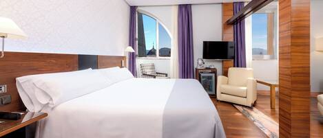 Habitación de hotel con una cama grande, un escritorio, una silla, televisión y vistas a la ciudad.