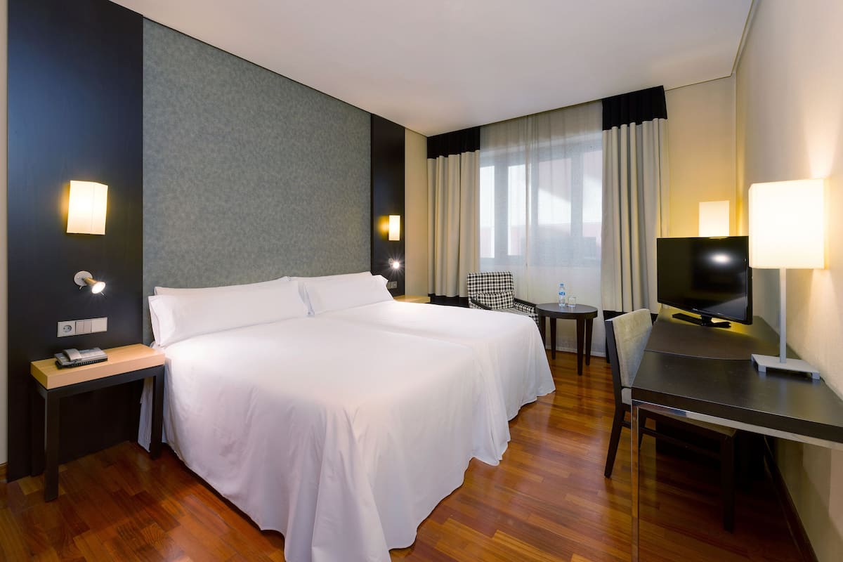 Une chambre d’hôtel avec un lit double, un bureau avec une chaise, une télévision et deux tables de chevet avec des lampes.