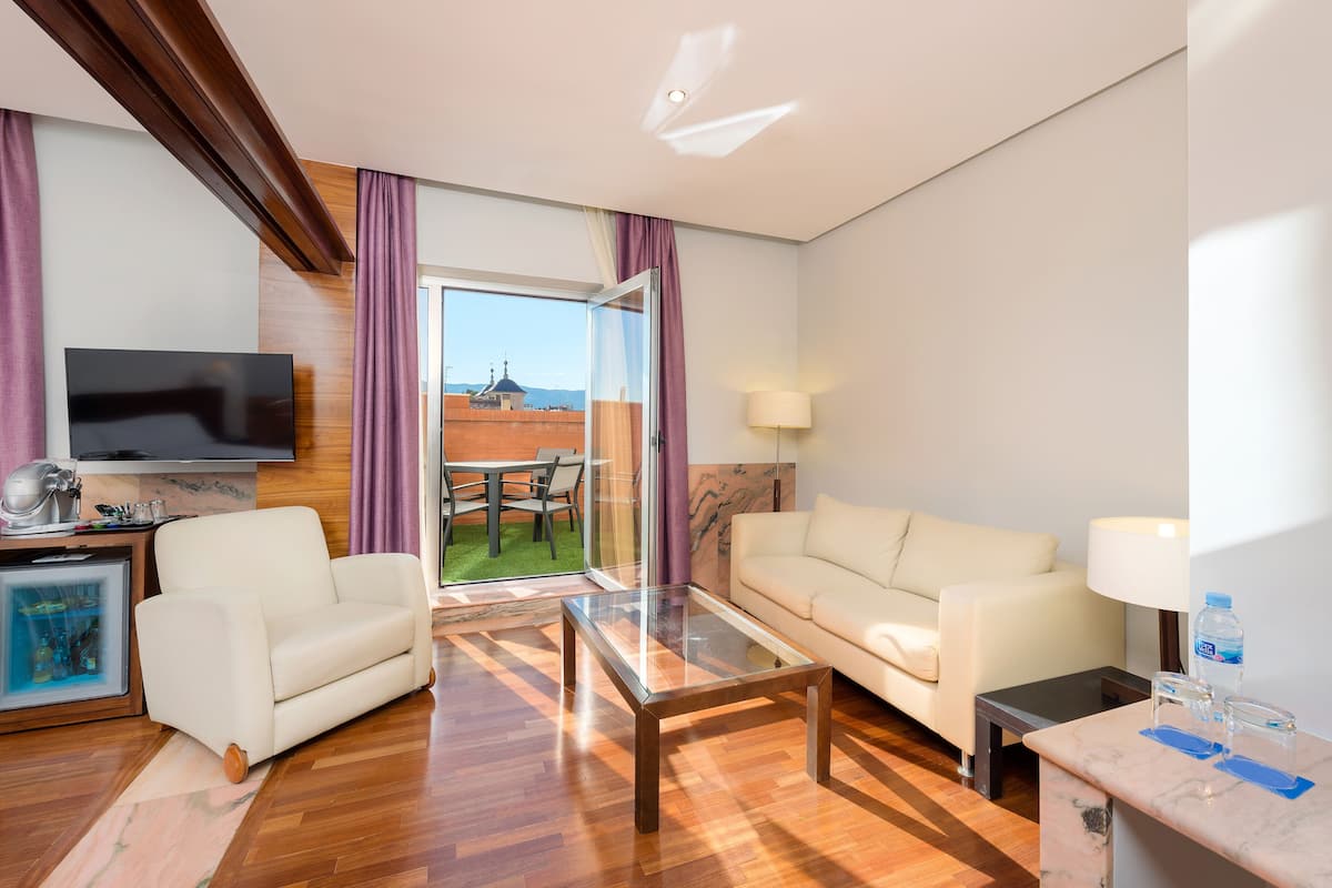 Une chambre d’hôtel moderne, dotée d’un canapé, d’une table basse en verre, d’un téléviseur et offrant une vue sur le paysage urbain par la fenêtre.