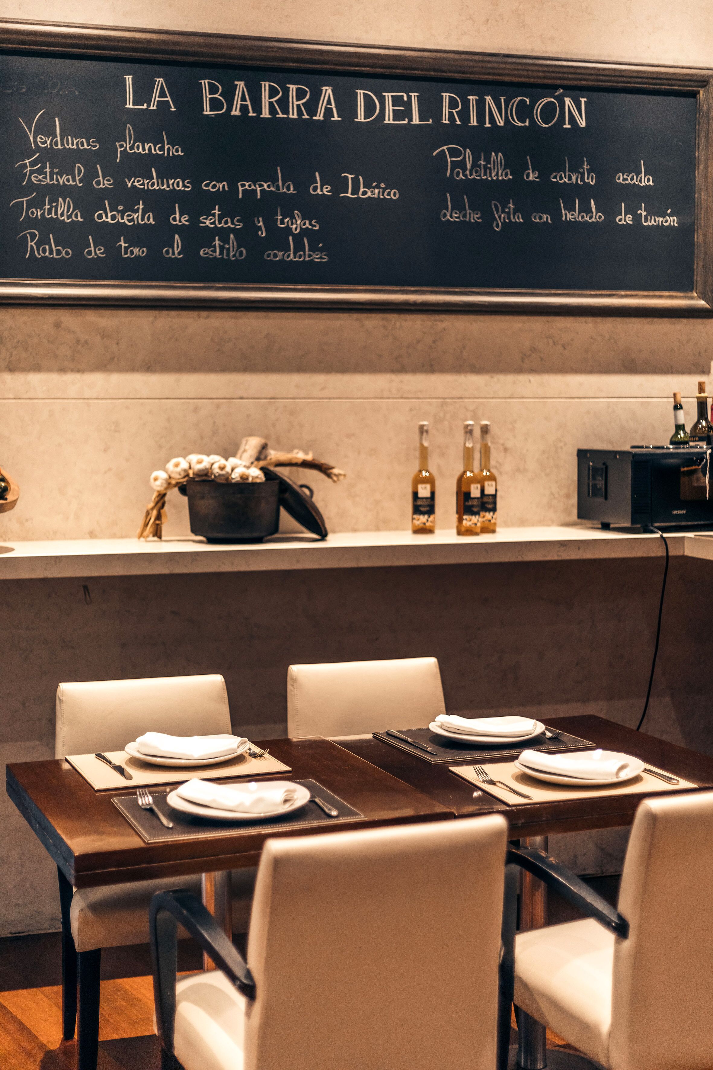 A restaurant interior with a chalkboard menu listing dishes like 'Verduras plancha' and 'Festival de verduras con papada de Ibirico'.