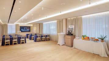 A conference room with a stage, rows of chairs, a buffet table, and a coffee station.