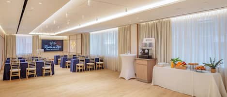 A conference room with a stage, rows of chairs, a buffet table, and a coffee station.