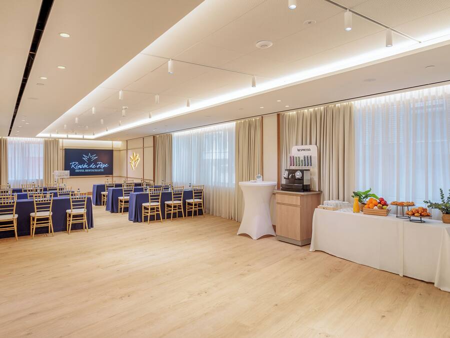 A conference room with a stage, rows of chairs, a buffet table, and a coffee station.
