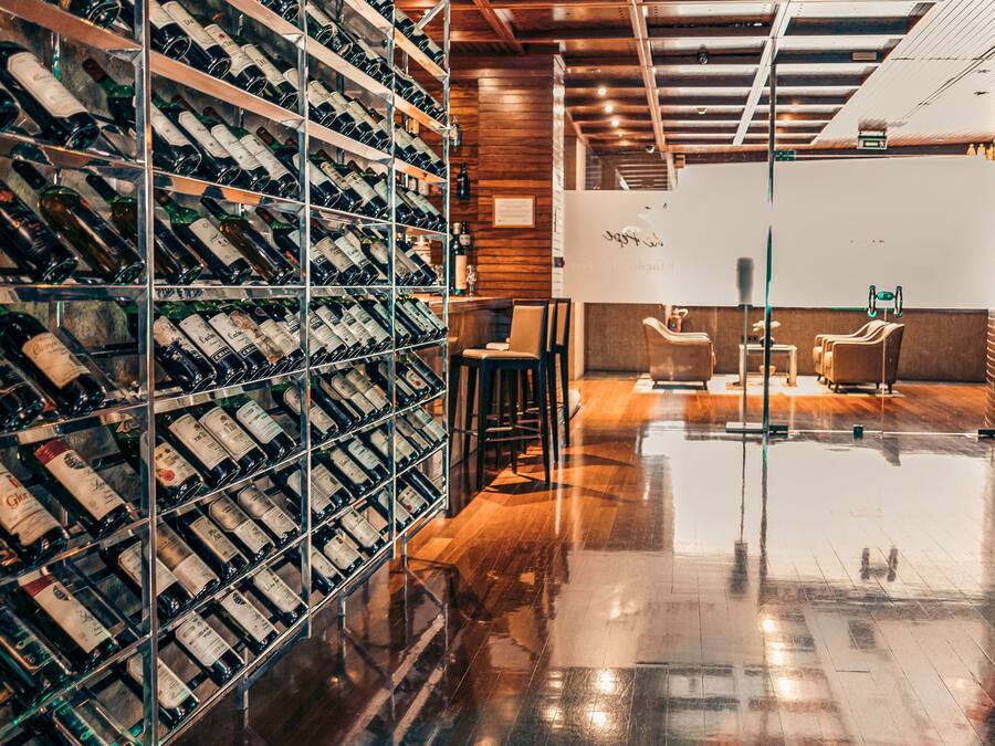 A wine cellar with shelves of wine bottles, a polished wooden floor, and a seating area with chairs and a table.
