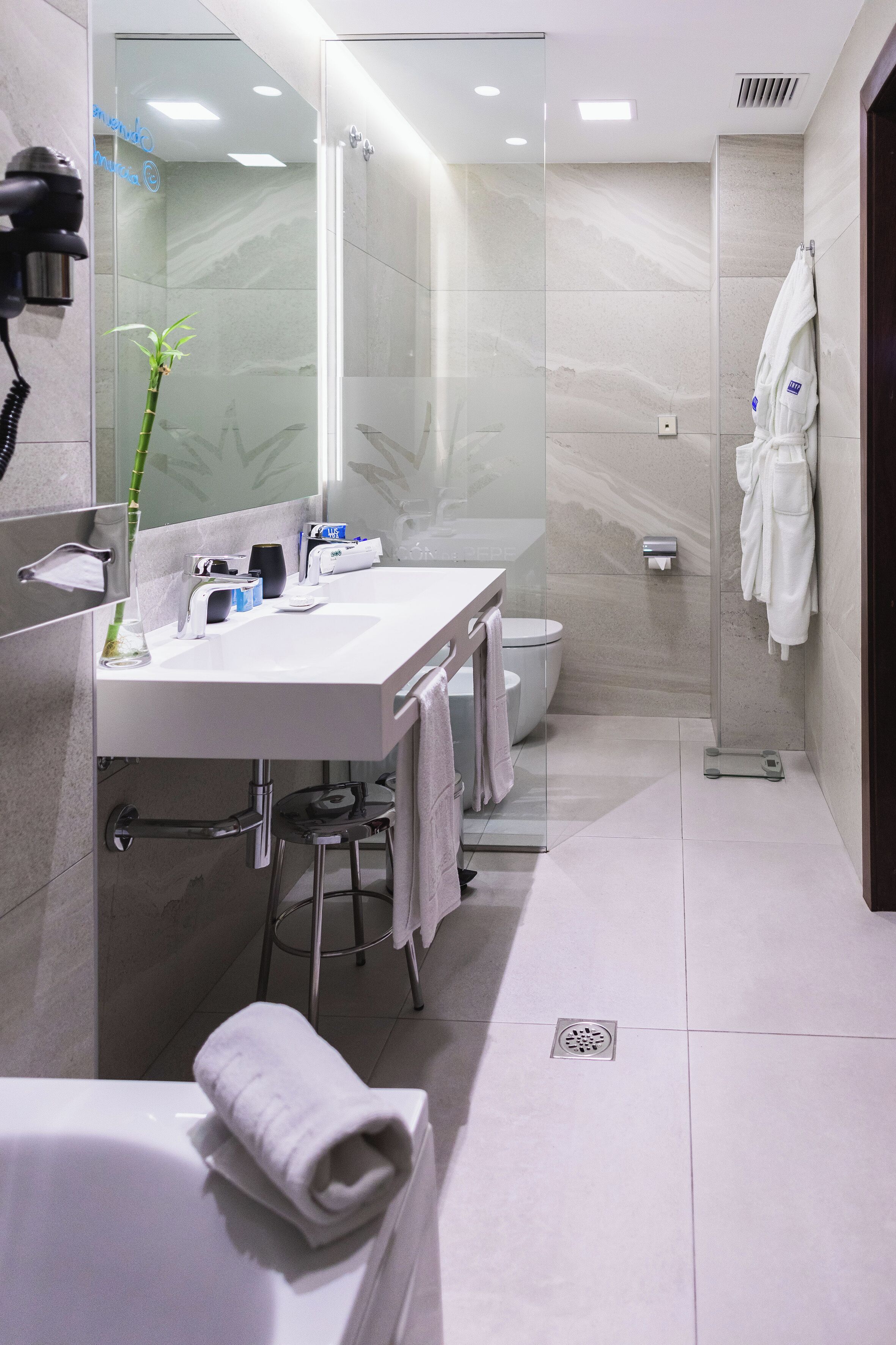 Un baño moderno con cabina de ducha de vidrio, un lavabo blanco con espejo y un perchero para toallas.