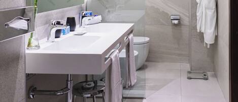 Un baño moderno con cabina de ducha de vidrio, un lavabo blanco con espejo y un perchero para toallas.