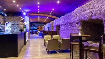 A modern bar area with a rustic stone wall, wooden ceiling, and seating arrangements.