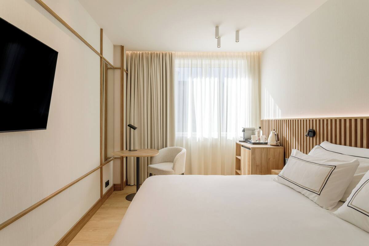 Une chambre d’hôtel avec un grand lit, un bureau avec une chaise, un téléviseur fixé au mur et une fenêtre avec des rideaux.