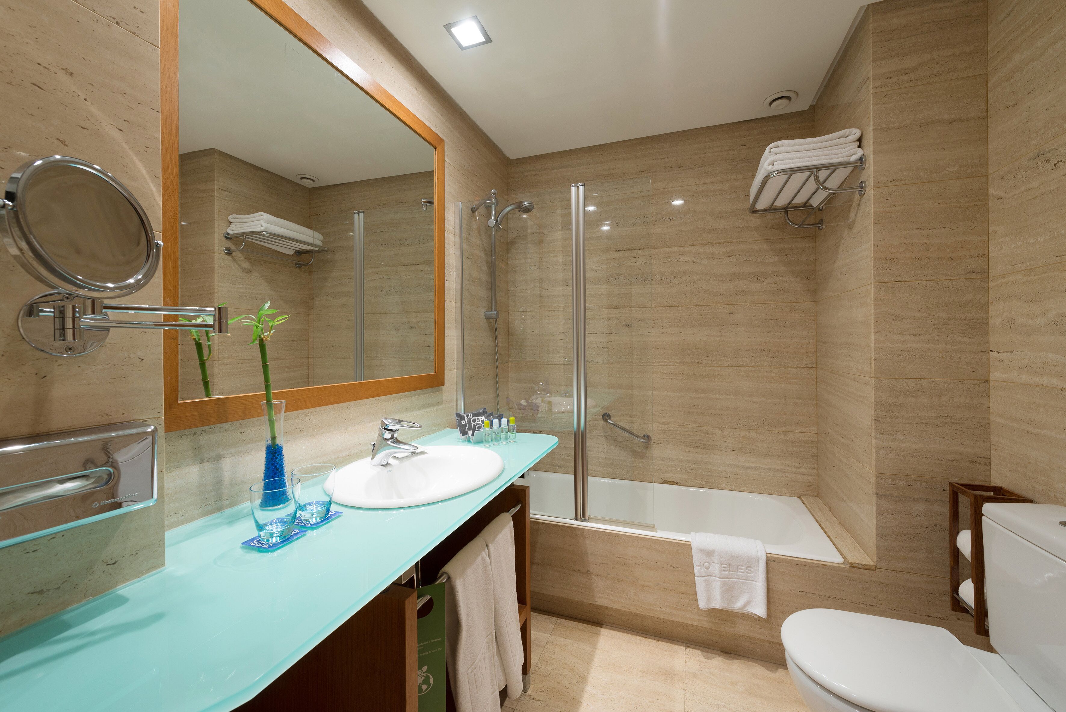 A modern bathroom with a glass sink, a large mirror, a glass-enclosed shower, and a white toilet.