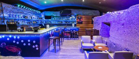 A bar area with a wooden bar counter, multiple seating options including bar stools and chairs, and a large rock feature.