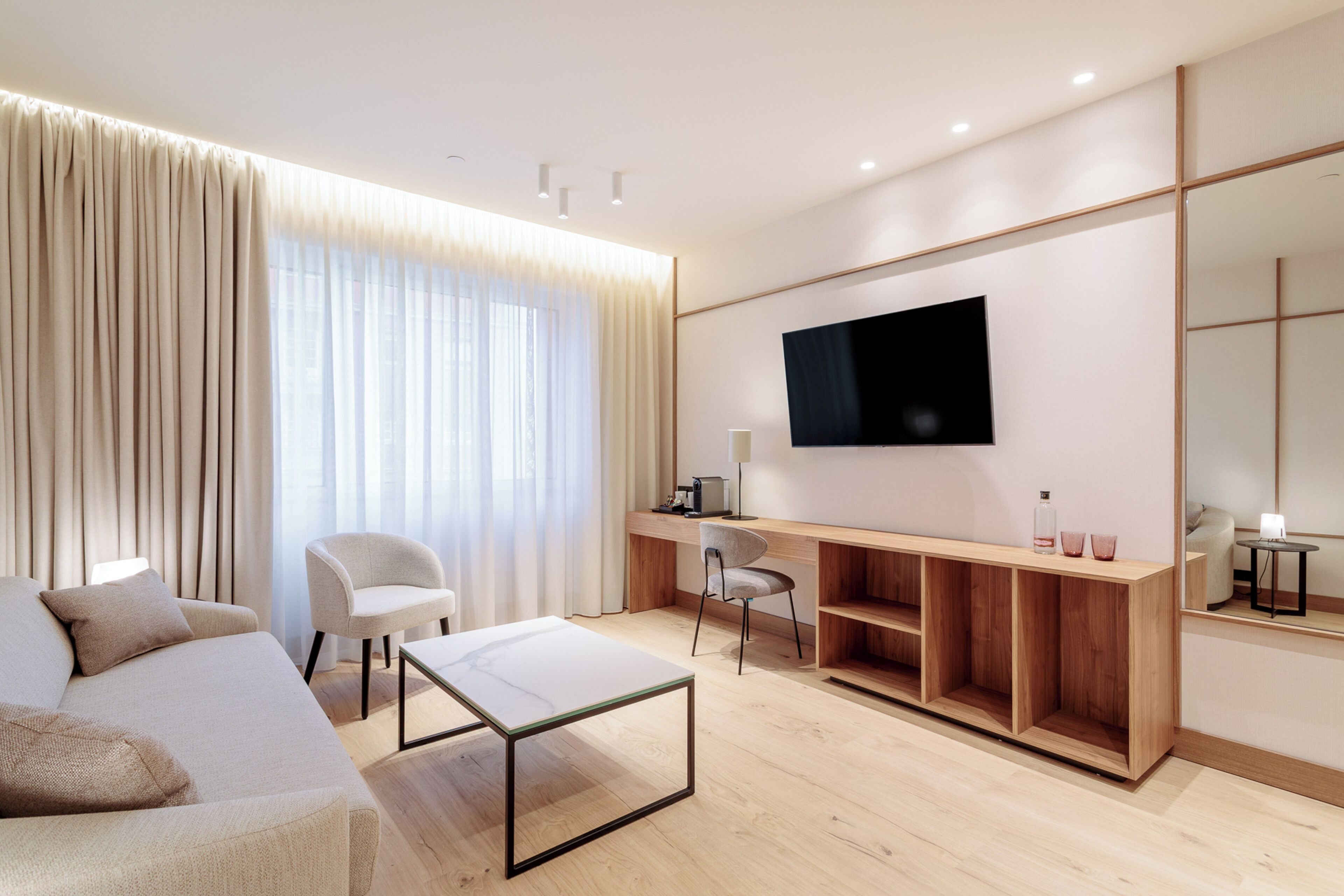 Una habitación de hotel moderna con sofá, escritorio, silla, televisor y un espejo grande.