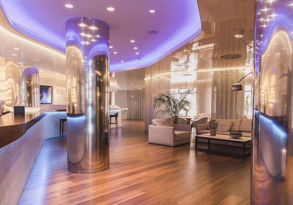 Un moderno vestíbulo de hotel con suelo de madera, un mostrador de recepción y un área de descanso con un sofá y una mesa de centro.