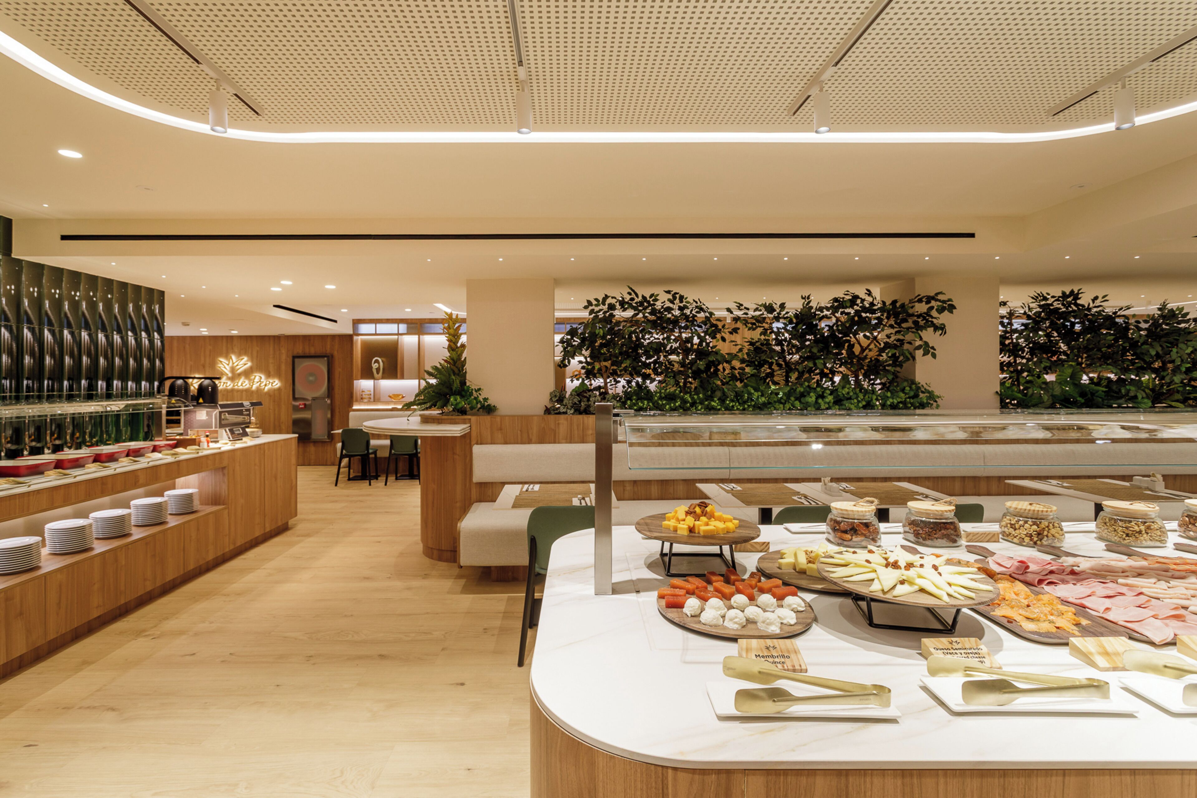 A buffet area with various food items, a seating area, and a decorative wall with greenery.