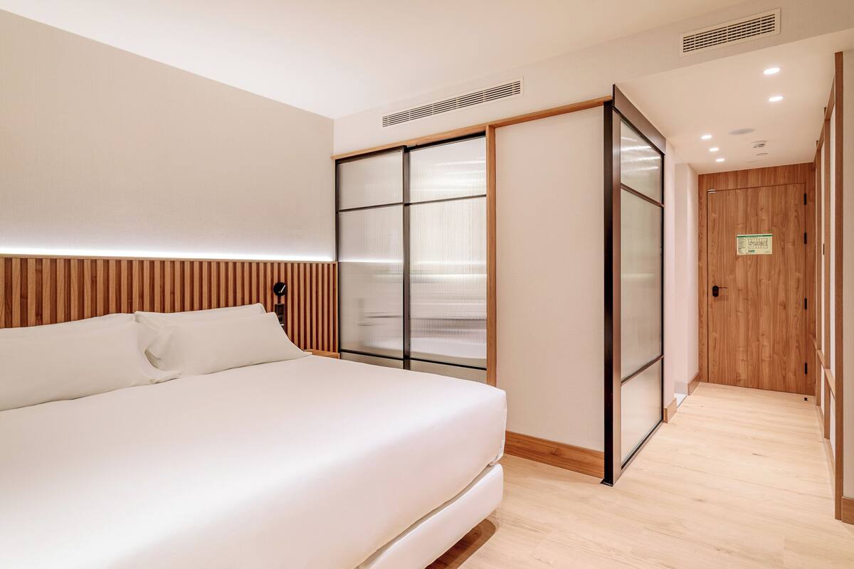 Une chambre moderne avec un grand lit, des portes-fenêtres coulissantes et un plancher en bois.