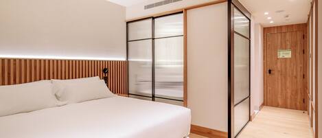 A modern bedroom with a large bed, sliding glass doors, and a wooden floor.