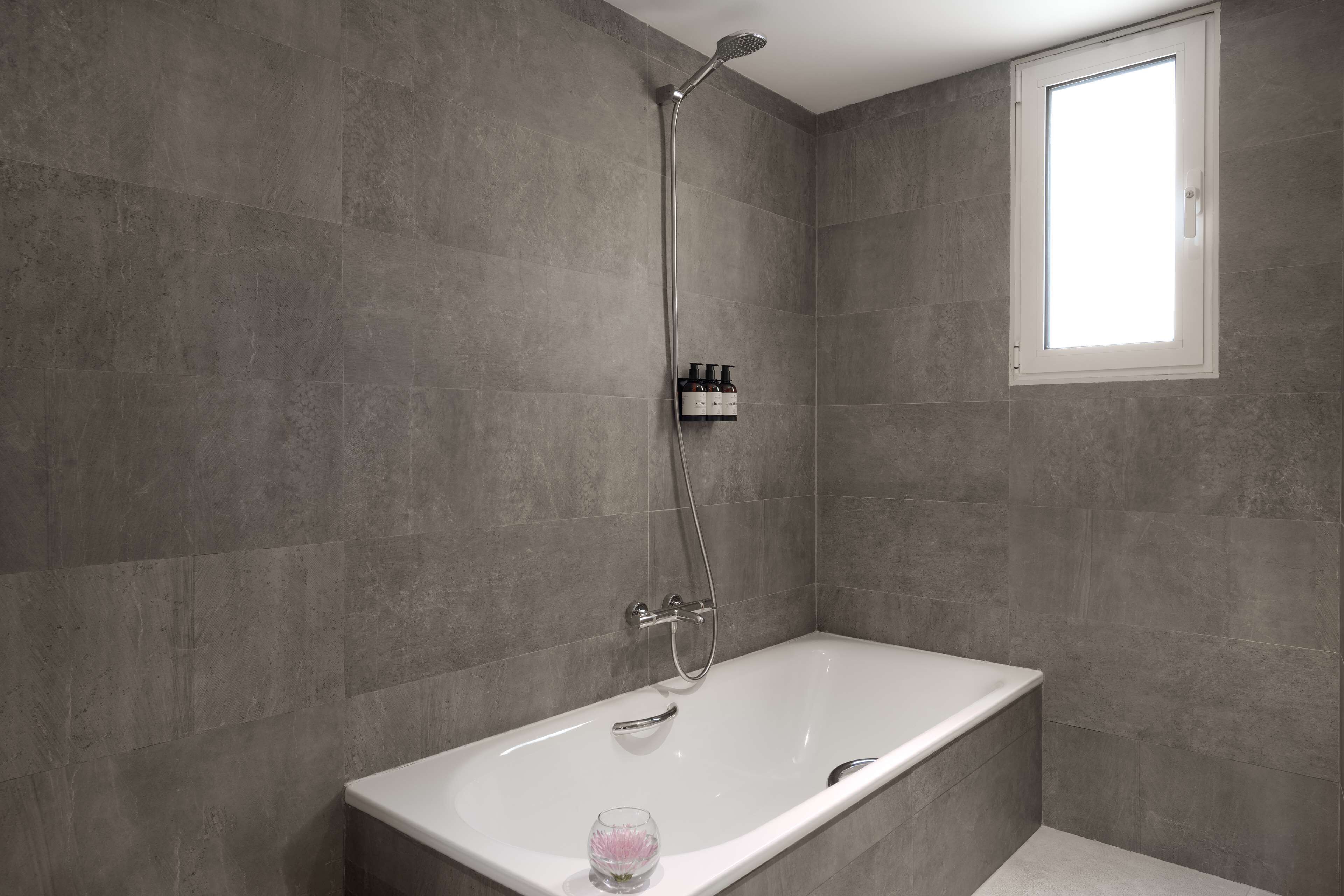 Un baño moderno con una bañera independiente, un cabezal de ducha de mano y un ventanal que proporciona luz natural.