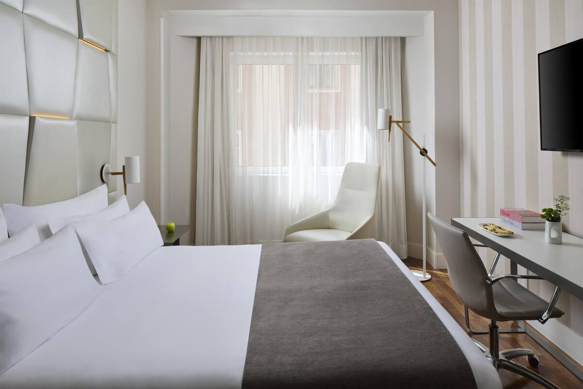A hotel room with a large bed, a desk, a chair, a television, and a window with curtains.