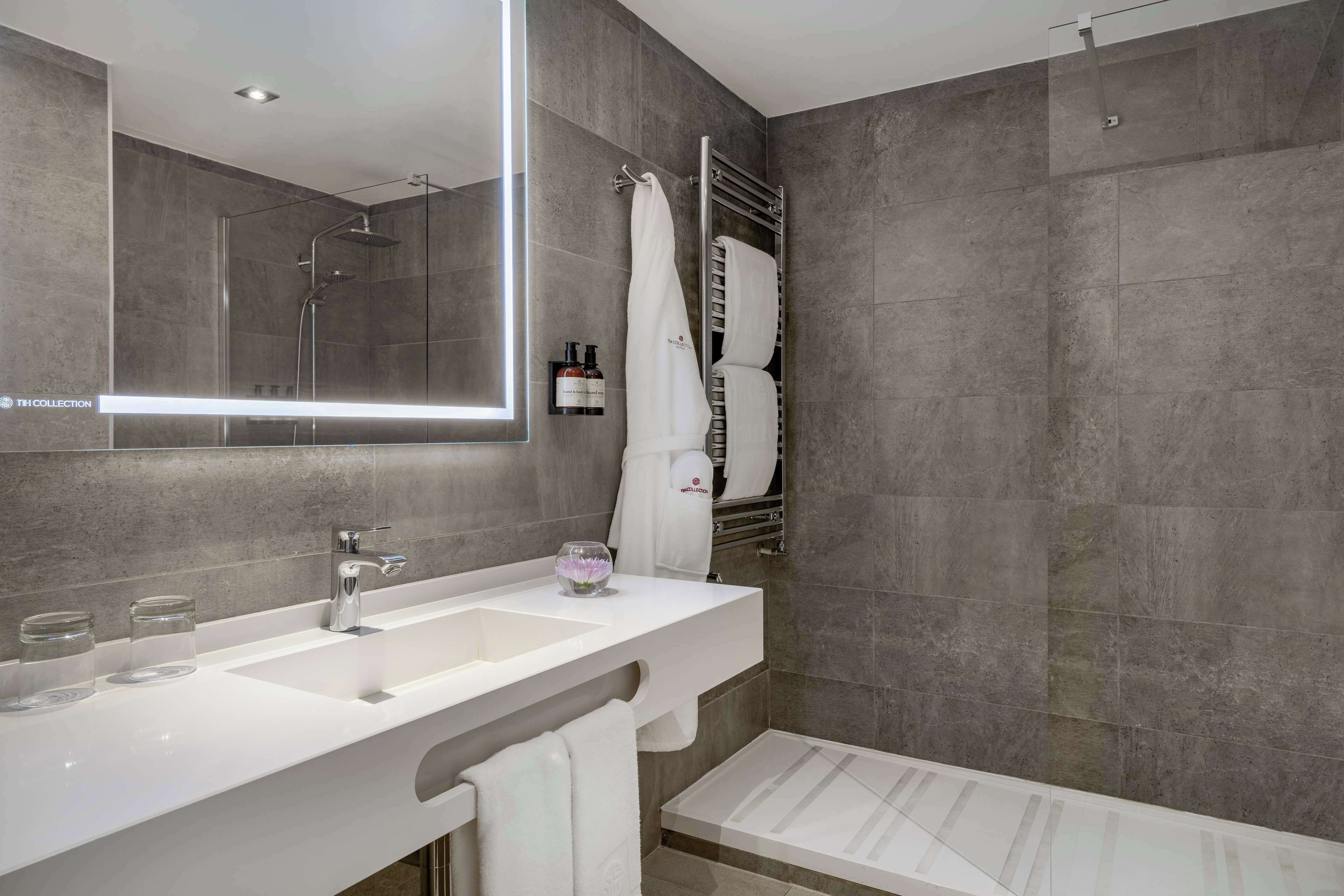 A modern bathroom with a large mirror, a shower, and a vanity with a sink and three glasses.