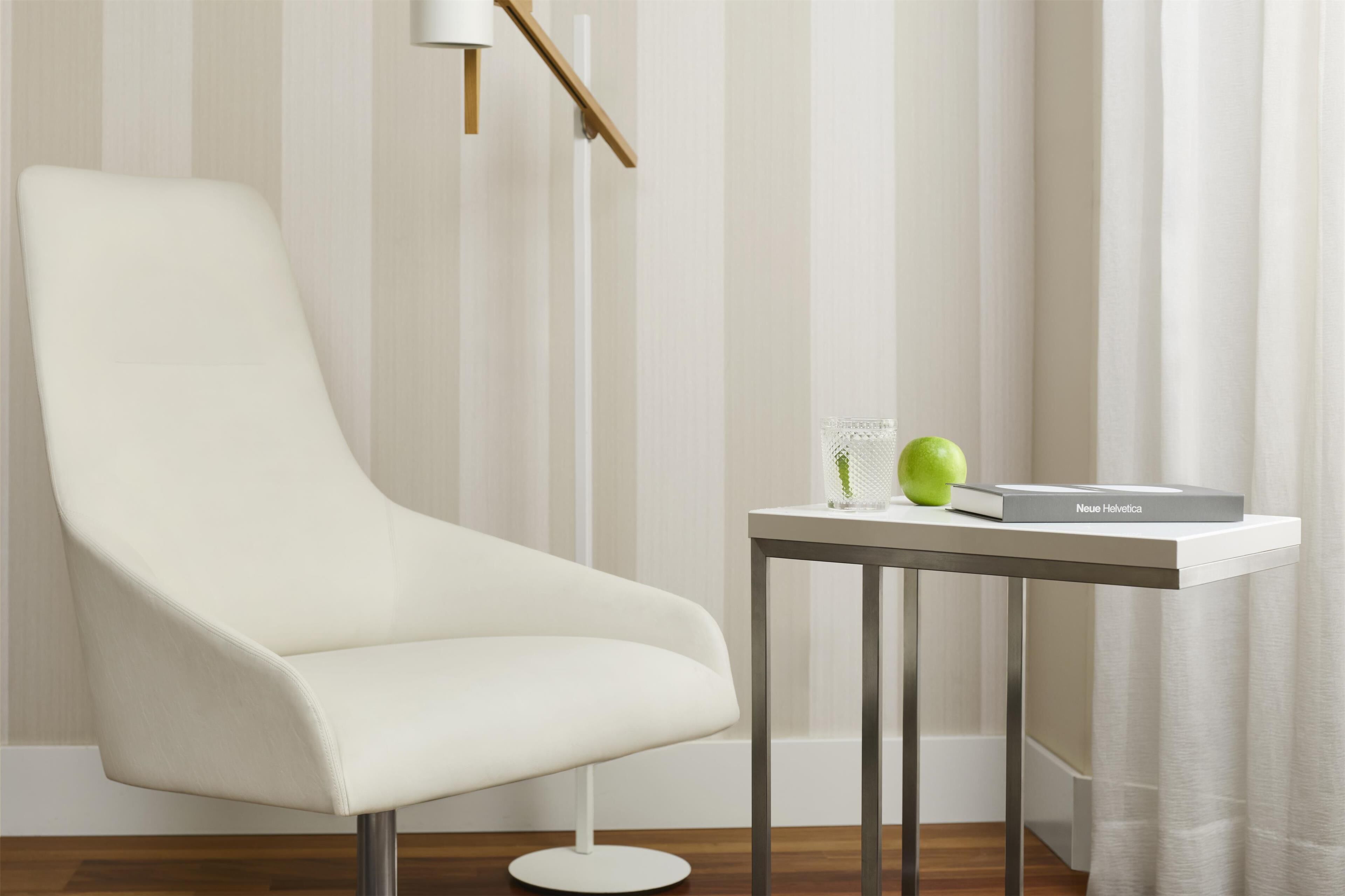 Una habitación moderna con un sillón blanco, una pequeña mesa con un libro y una manzana verde, y una lámpara de pie.