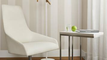 Una habitación moderna con un sillón blanco, una pequeña mesa con un libro y una manzana verde, y una lámpara de pie.