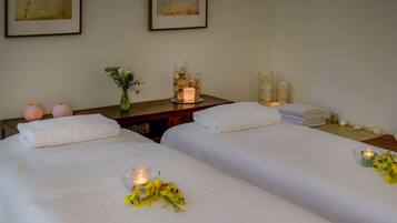 Una habitación de hotel con dos camas, una mesita de noche con velas, un florero con flores y toallas apiladas con cuidado.