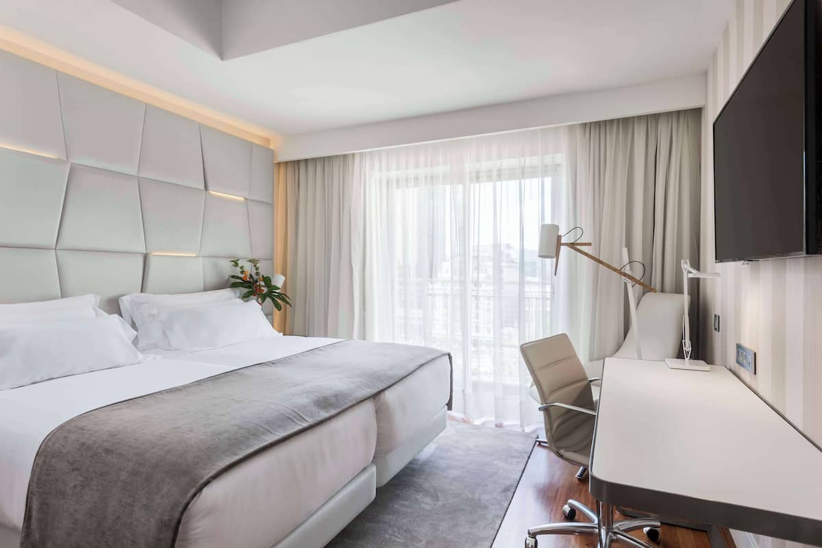 A modern hotel room with a large bed, a desk, and a TV.
