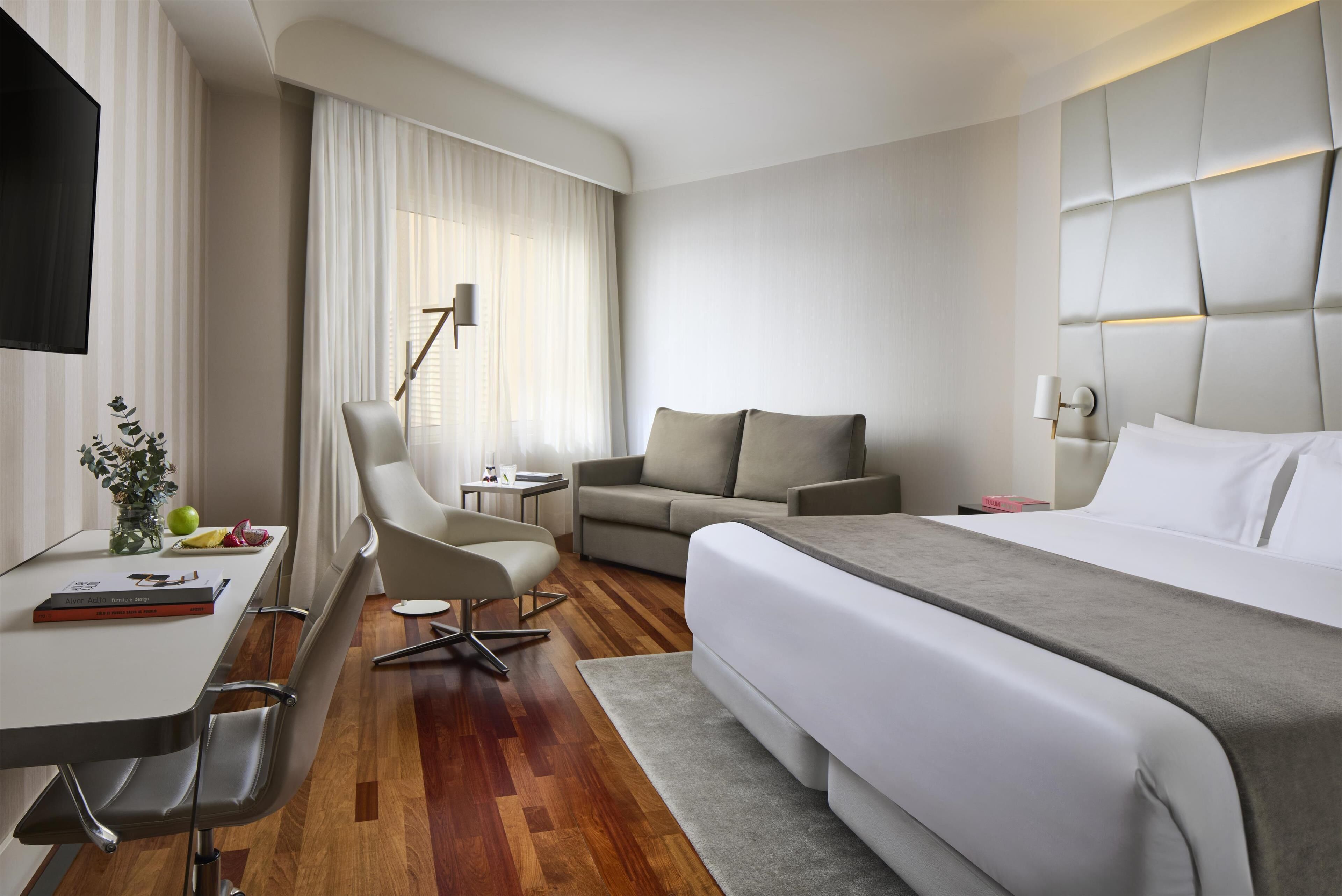 Una habitación de hotel moderna con cama, escritorio, sillón, sofá y televisión.