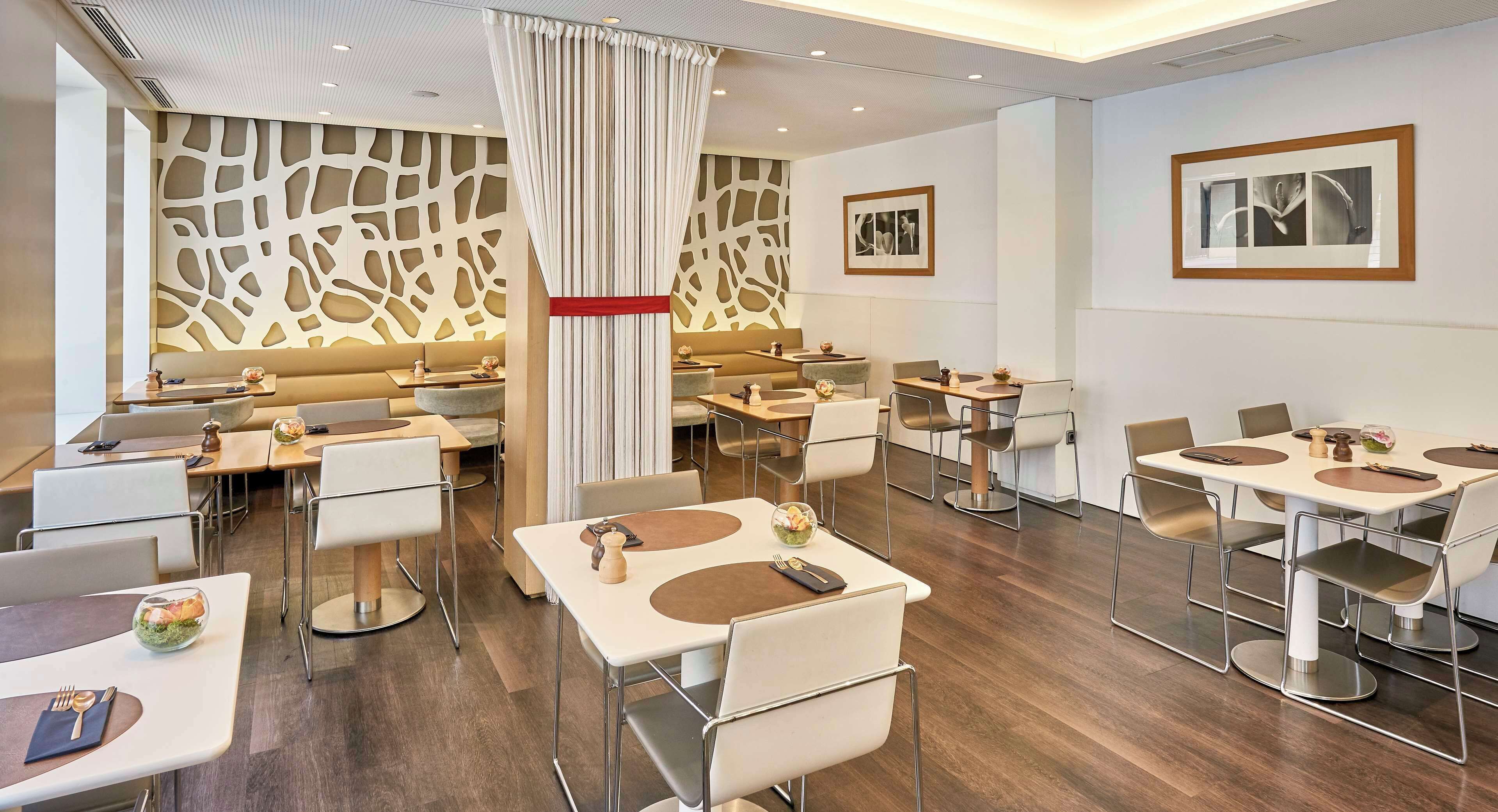 Un comedor moderno de hotel con varias mesas y sillas, una columna decorativa central y arte abstracto en las paredes.