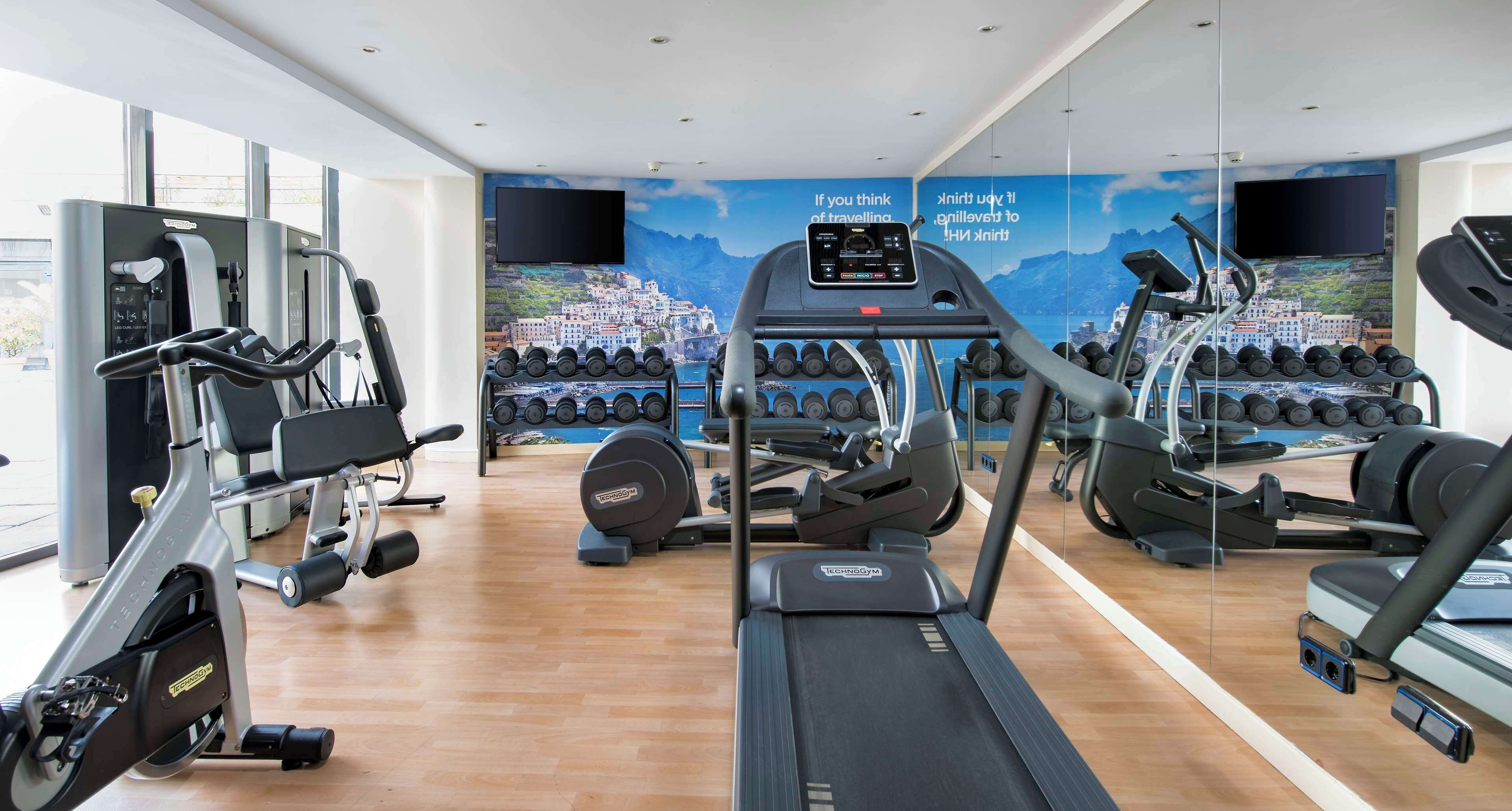 Una palestra con macchinari cardio, pesi e un murale panoramico.