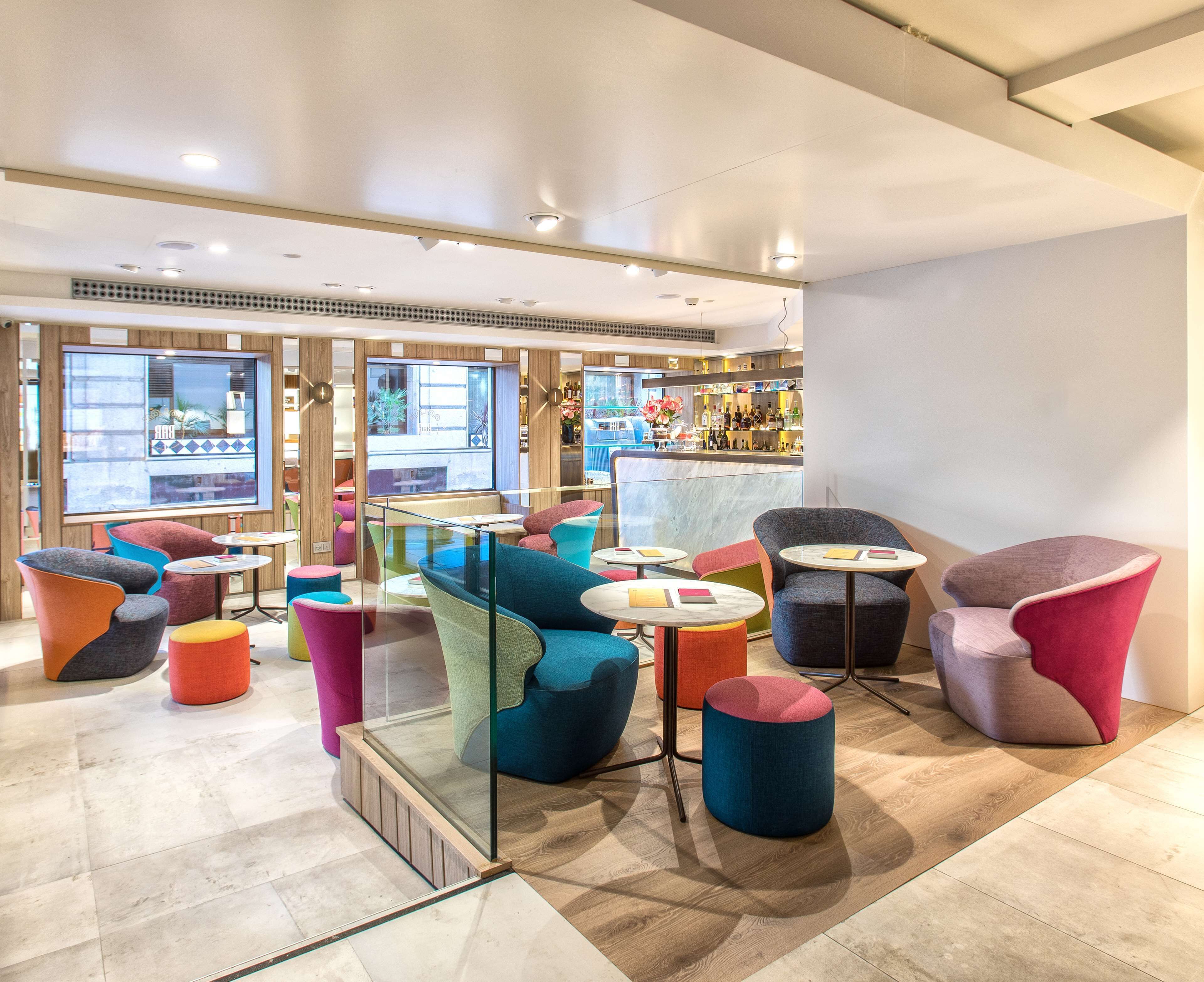 Una zona relax moderna con sedute colorate, una parete divisoria in vetro e un bar sullo sfondo.