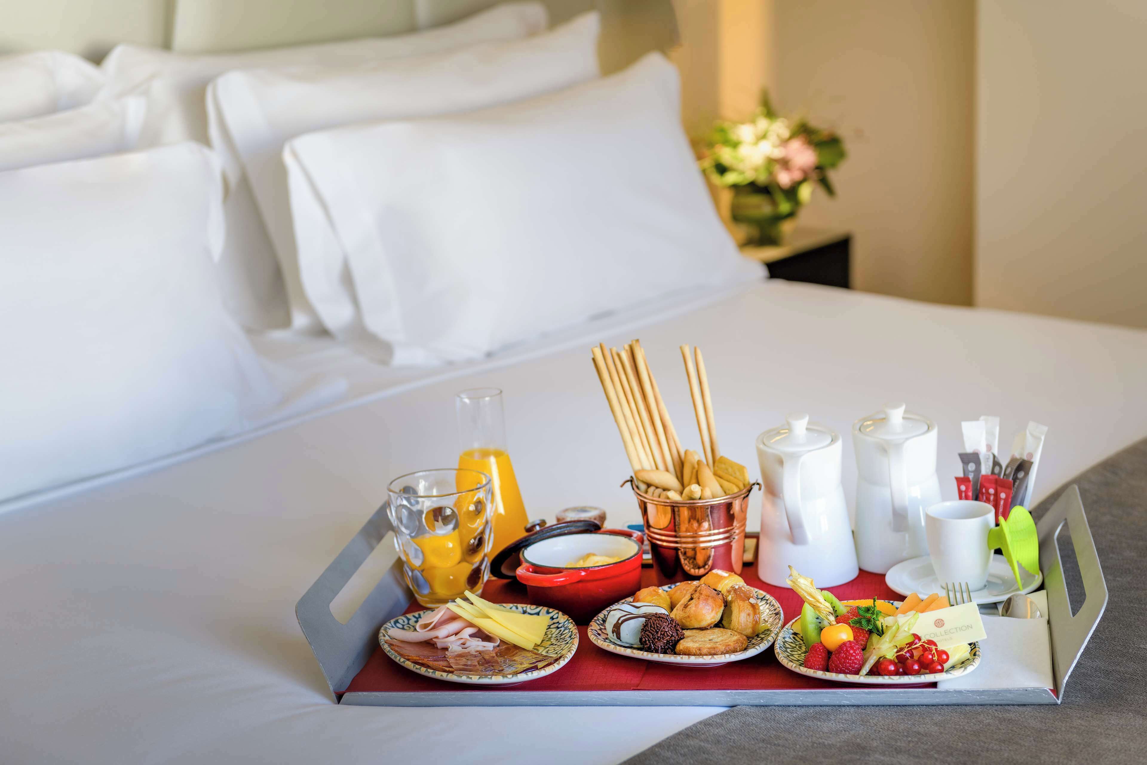 A breakfast tray with various foods and drinks on a bed in a hotel room.