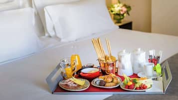 A breakfast tray with various foods and drinks on a bed in a hotel room.