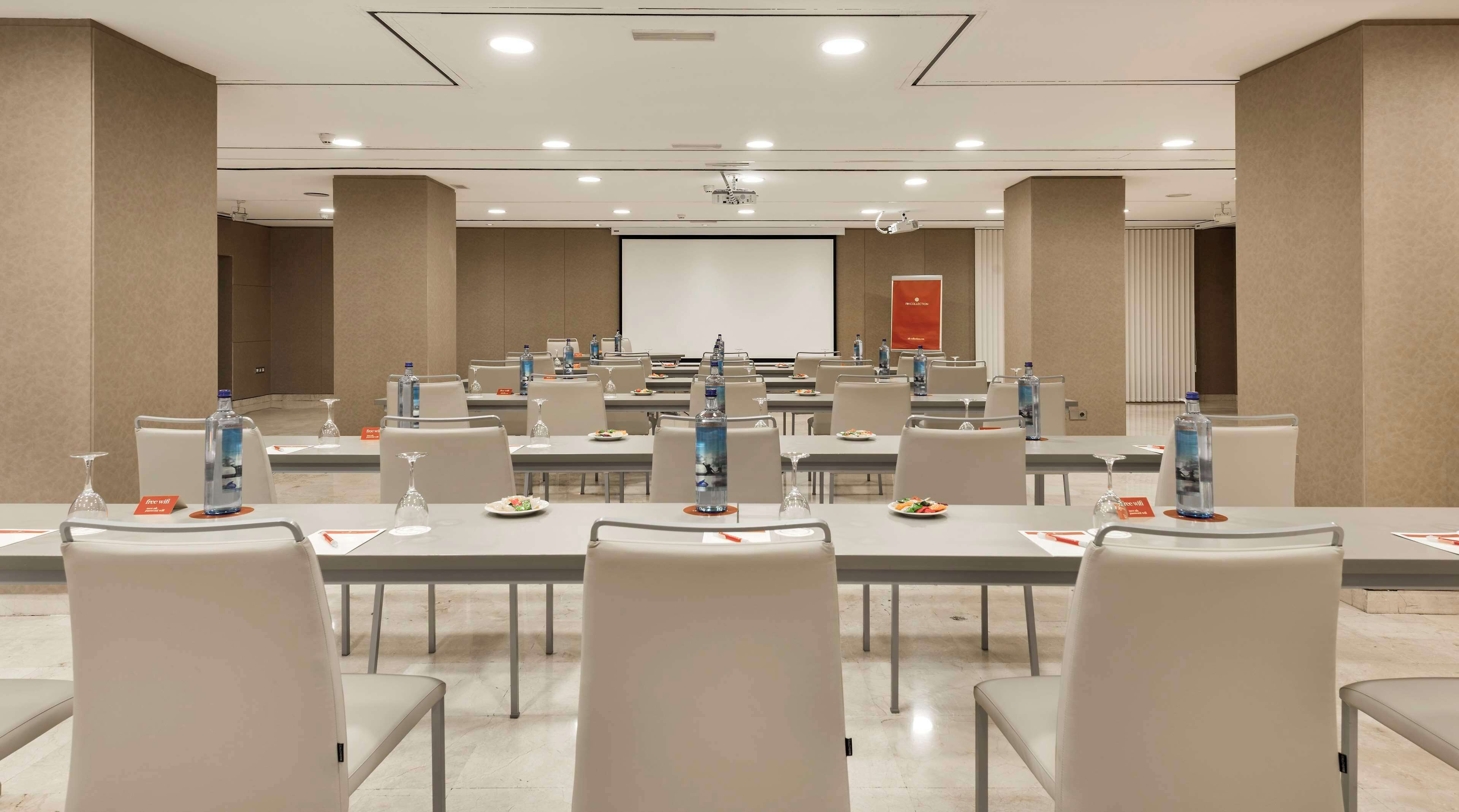 Un salón de conferencias con varias mesas, sillas, botellas de agua y tarjetas de identificación.