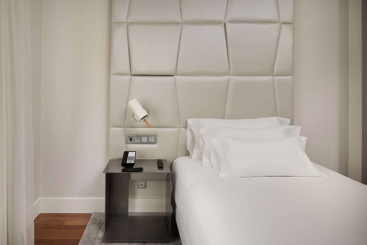 A hotel room with a large bed, a bedside table with a lamp, and a phone.