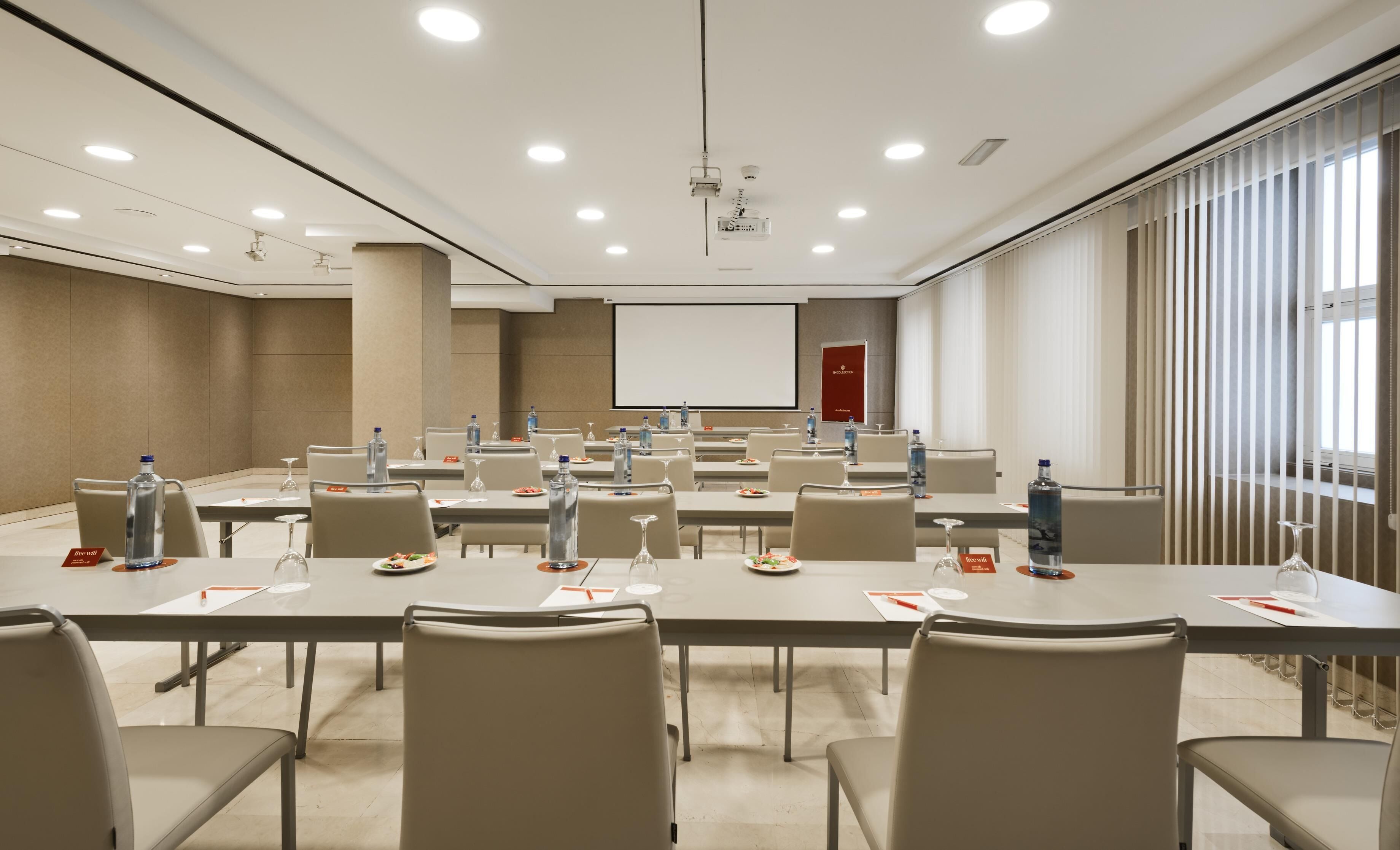 A conference room with tables, chairs, water bottles, and a projector screen.