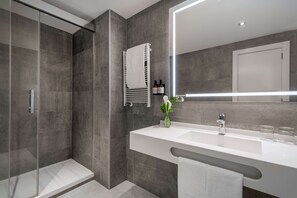 A modern bathroom with a glass-enclosed shower, a large mirror, and a white vanity with a sink and towel rack. - NH Collection Madrid Colón (Madrid)