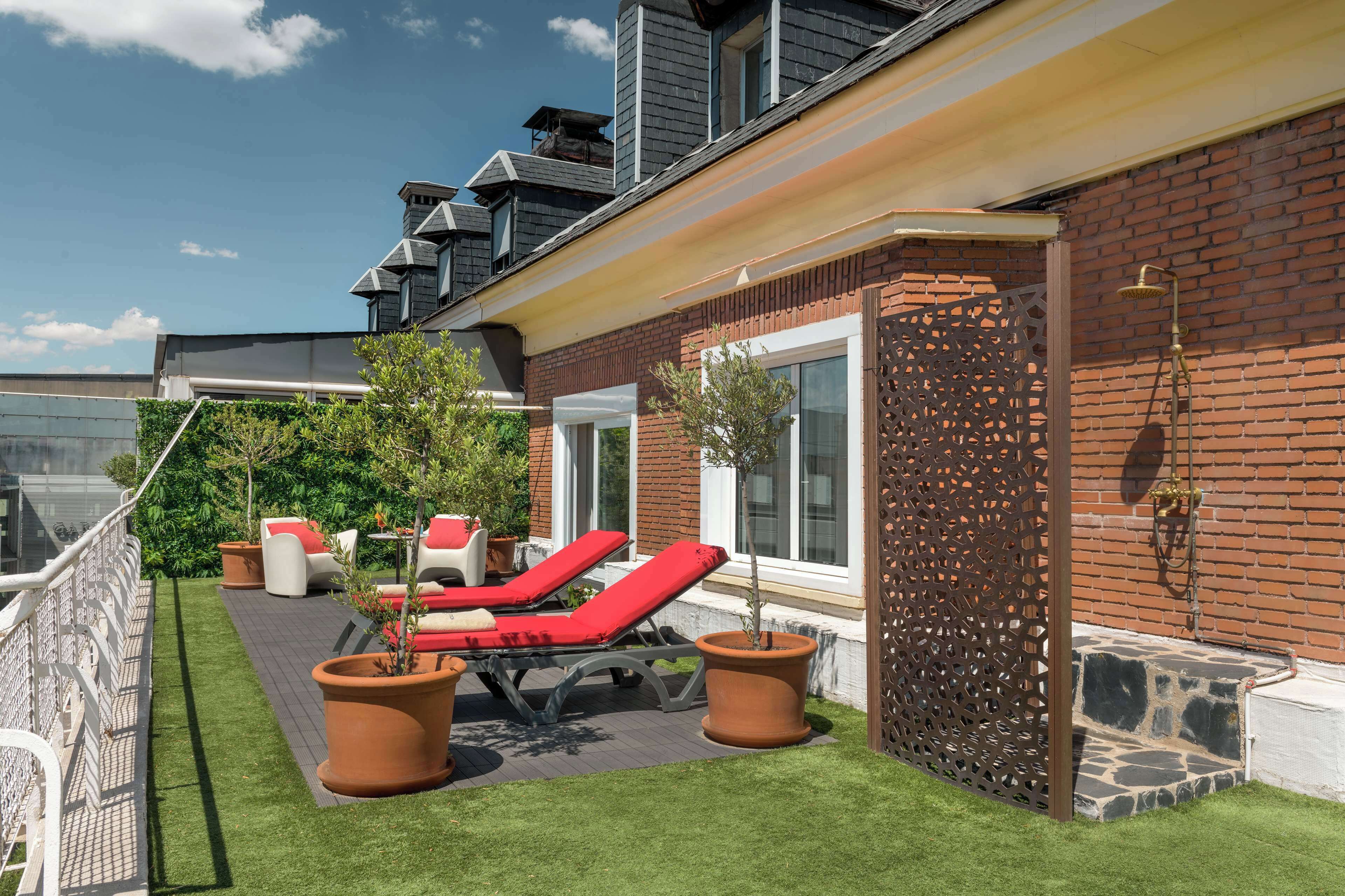 Una terrazza sul tetto con poltrone rosse, una piccola area giardino e un muro in mattoni con un pannello decorativo.
