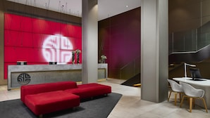 Un moderno hall de entrada con un mostrador de recepción rojo, un sofá y un escritorio con dos sillas.