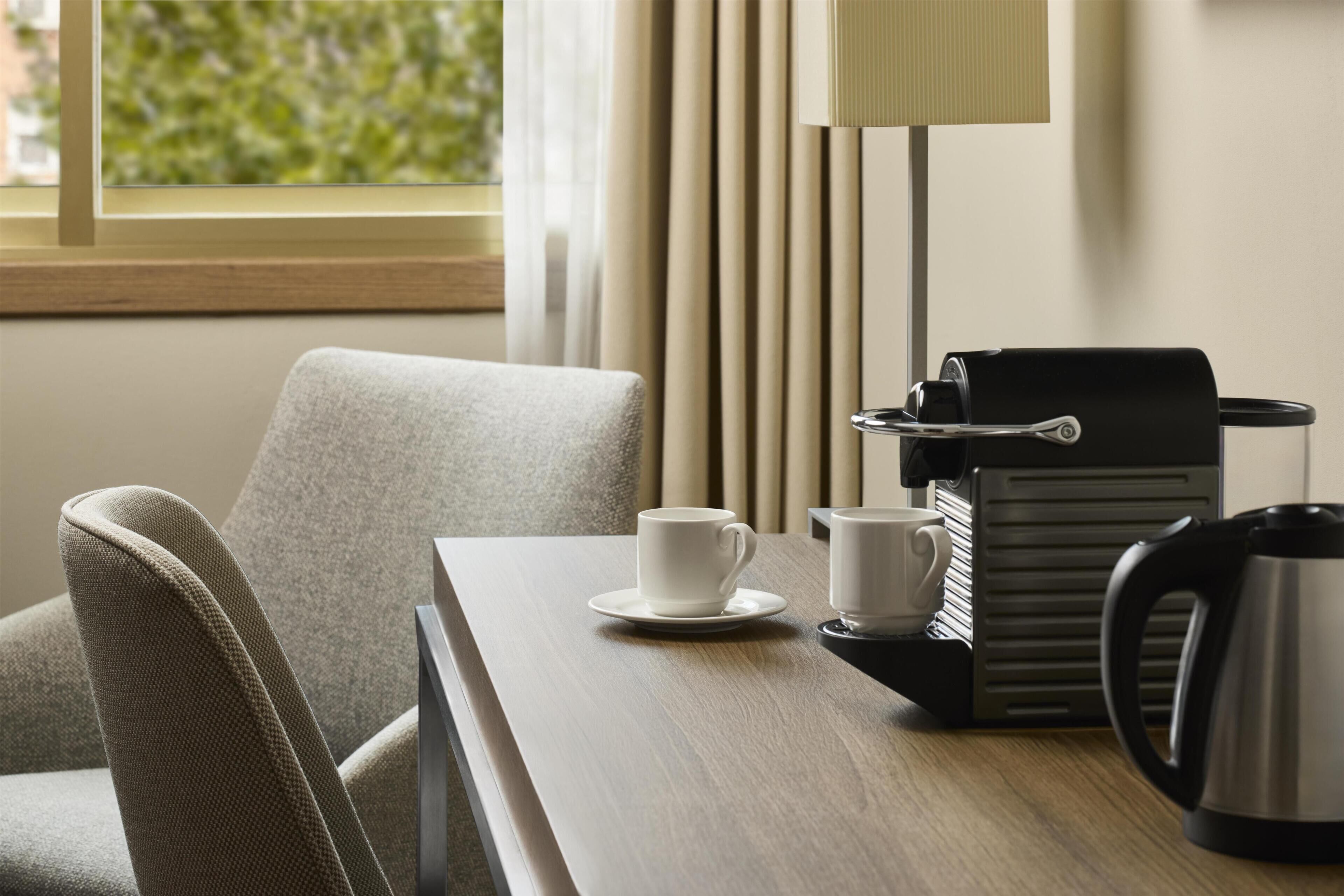 Ein Hotelzimmer mit Holztisch, weißer Tasse, Kaffeemaschine und Wasserkocher.