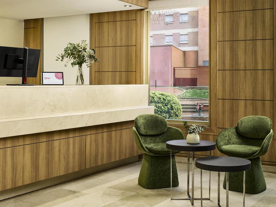 Un área de recepción con un mostrador de madera, dos sillones tapizados de color verde, una mesita y un monitor.