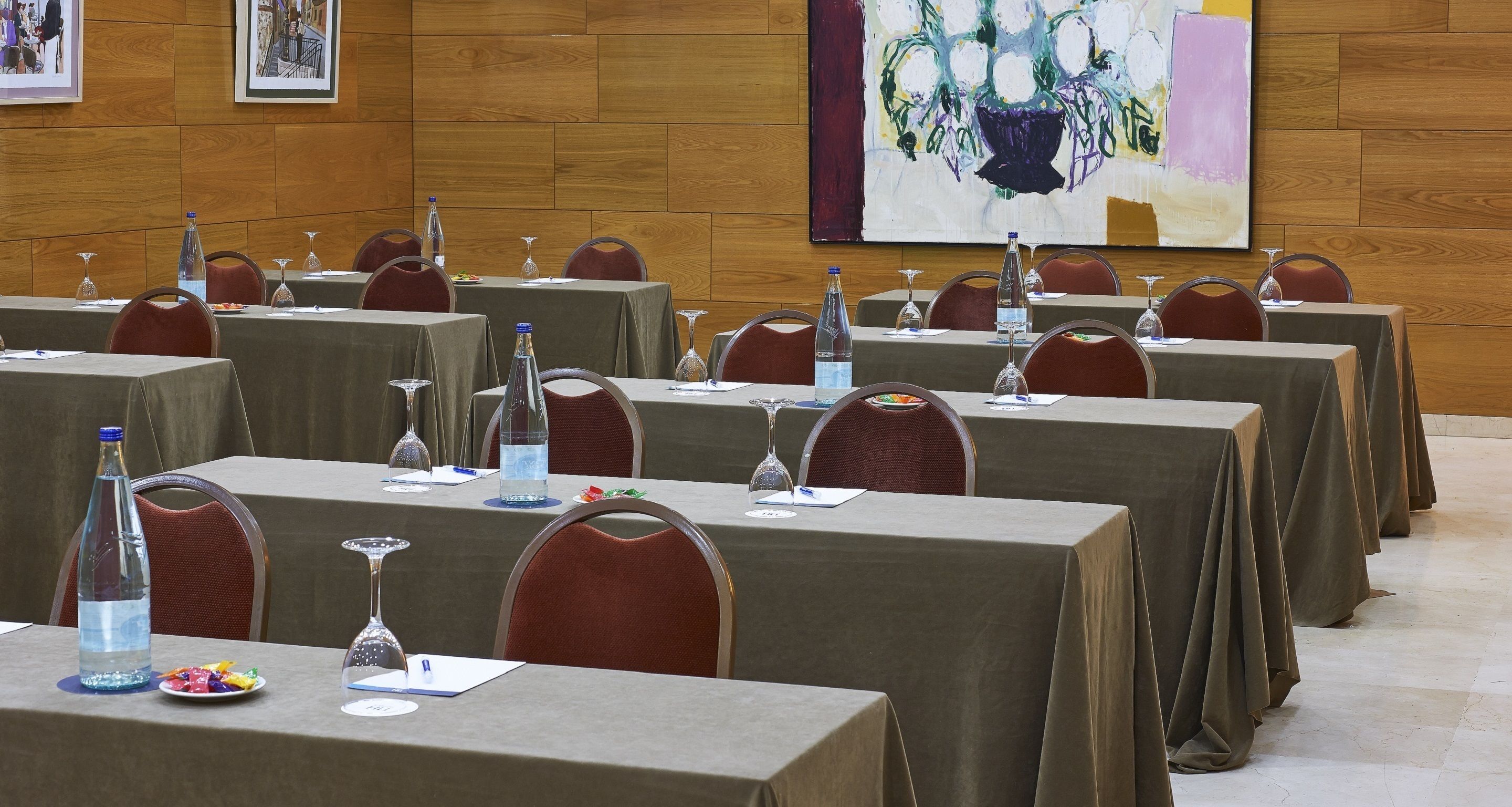 Un salón de conferencias con varias mesas, cada una con botellas de agua, vasos y blocs de notas.