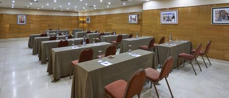 Un salón de conferencias con varias mesas y sillas, equipado con botellas de agua y documentos.