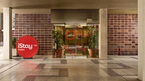A hotel entrance with a red logo, glass doors, potted plants, and a tiled floor.