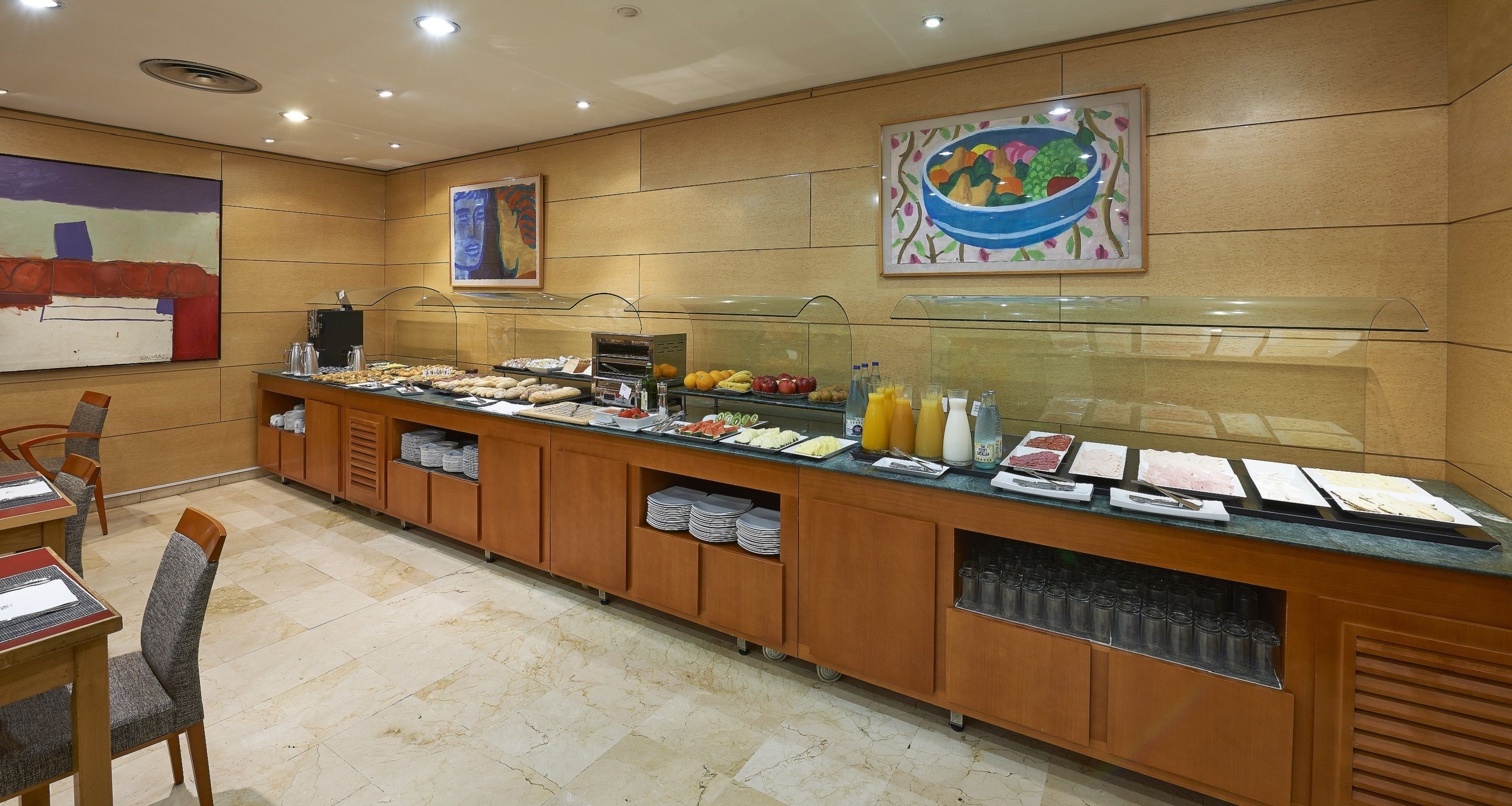 A buffet with various food items, a glass display case, and seating area with chairs.