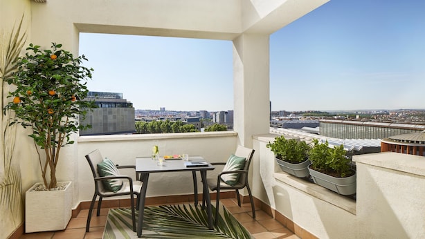 Ein Balkon mit Tisch und Stühlen, Blumentöpfen und Blick auf die Stadt.