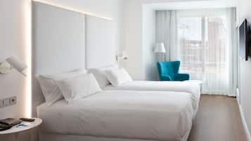 Quarto de hotel com duas camas, televisão, abajur e janela com cortinas.