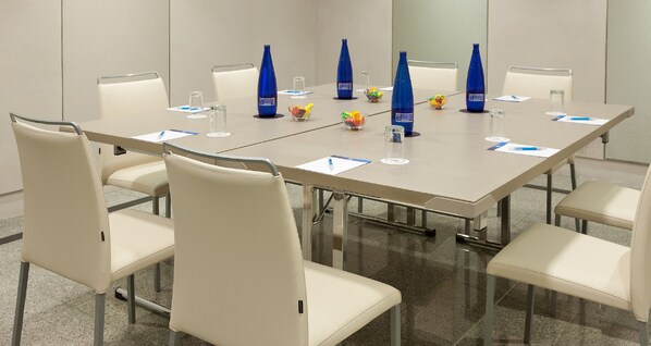 Un salón de conferencias con una larga mesa, sillas blancas y botellas de agua azules.