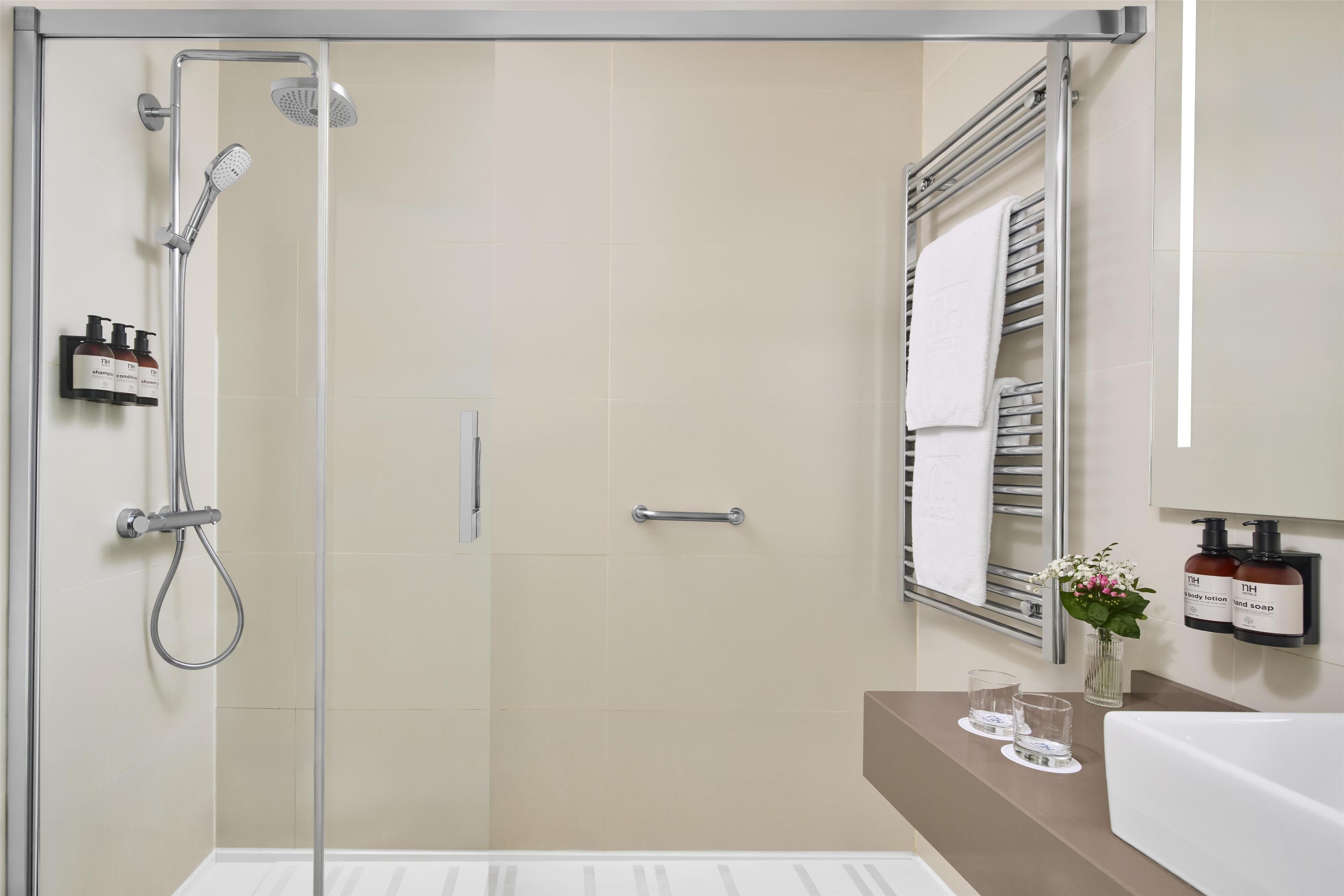 Een moderne badkamer met een douchecabine van glas, een handdoekrek, een wastafel met spiegel en toiletartikelen aan de muur.